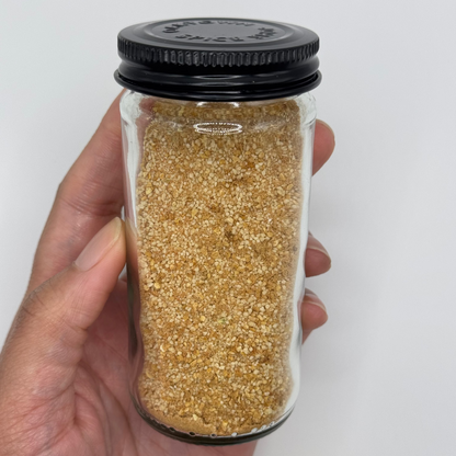 Hand holding a glass jar with black lid containing a brown granular substance on a white background