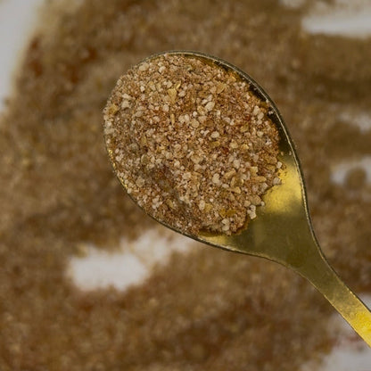 Gold spoon filled with brown powder against a blurred brown background